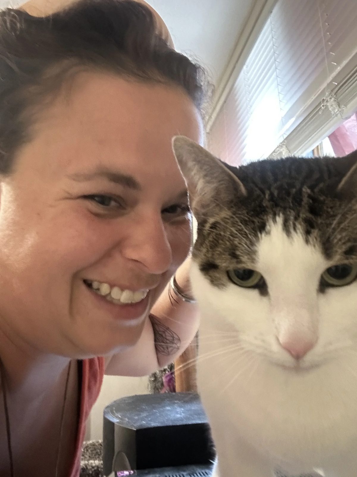 Lauren smiling widely in a selfie next to a white and tabby cat looking at the camera
